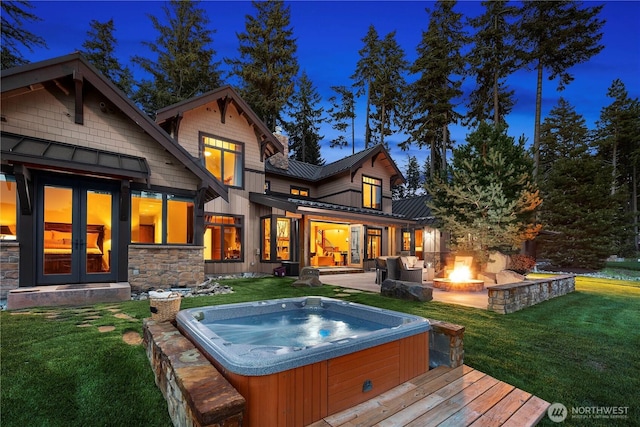 back of house with a lawn, an outdoor fire pit, a standing seam roof, and an outdoor hot tub