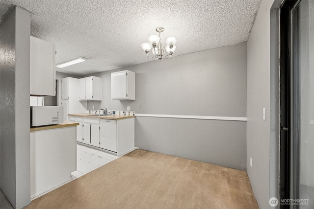 kitchen featuring a chandelier, light carpet, white cabinets, white appliances, and a sink