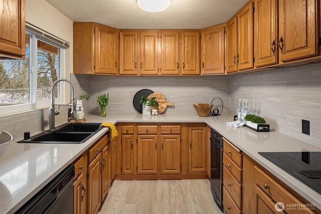 kitchen with black appliances, brown cabinetry, a sink, and light countertops