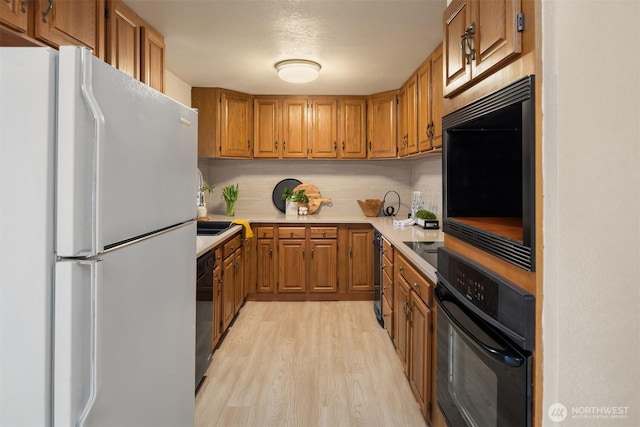 kitchen with brown cabinets, light wood finished floors, light countertops, backsplash, and black appliances