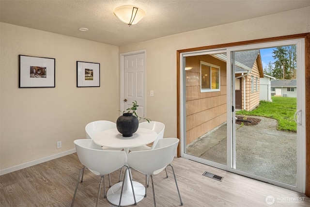 dining room featuring a textured ceiling, light wood finished floors, visible vents, and baseboards