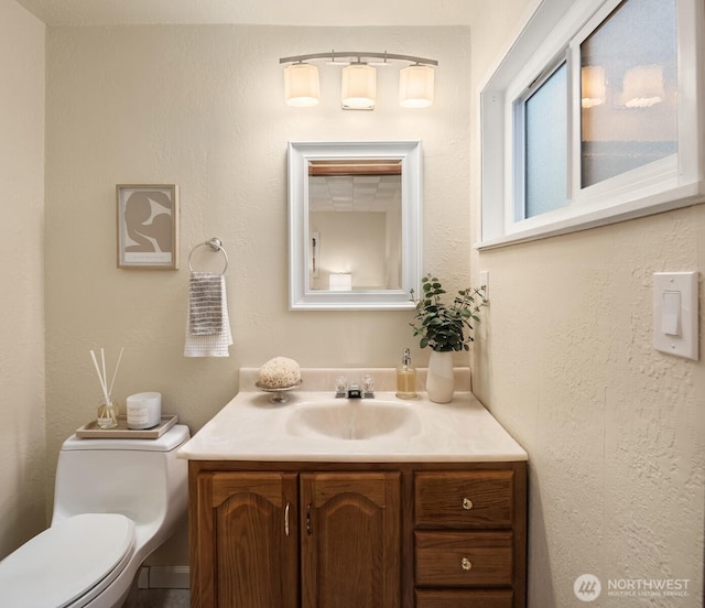 bathroom with a textured wall, vanity, and toilet