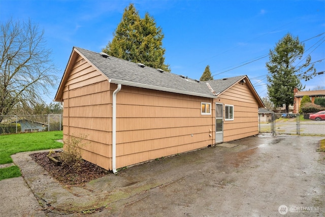 view of side of home with a shingled roof, a gate, fence, and a lawn