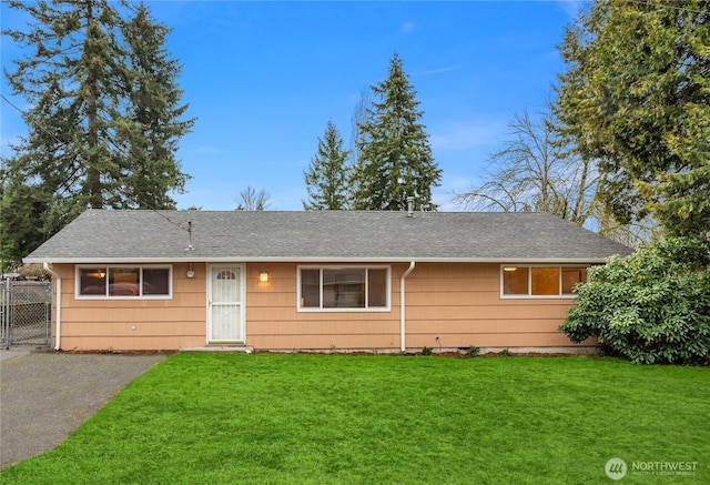 ranch-style home with driveway, a front lawn, a shingled roof, and fence