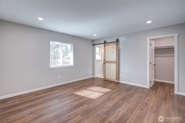 unfurnished bedroom with a barn door, baseboards, wood finished floors, a walk in closet, and recessed lighting