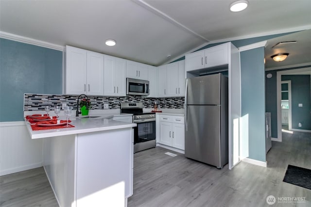 kitchen with light countertops, appliances with stainless steel finishes, white cabinets, a sink, and a peninsula