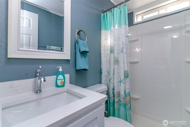 bathroom featuring a textured wall, curtained shower, vanity, and toilet