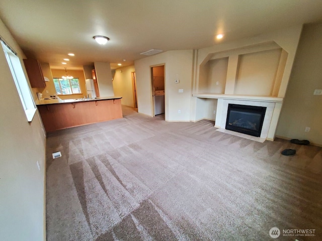 unfurnished living room featuring a chandelier, carpet, a fireplace with flush hearth, and recessed lighting