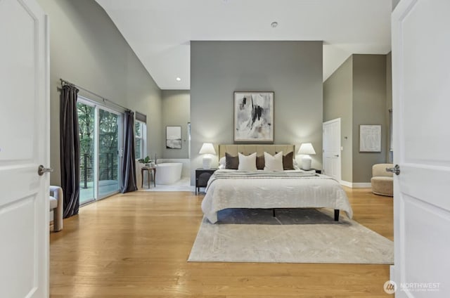 bedroom with access to outside, a high ceiling, baseboards, and wood finished floors