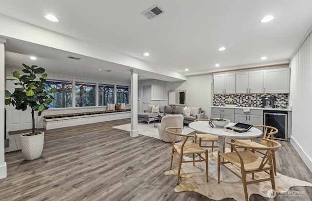 dining area featuring beverage cooler, indoor bar, wood finished floors, and visible vents