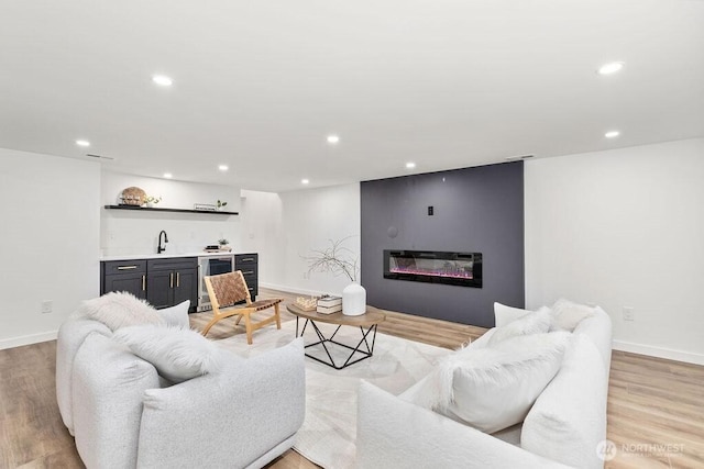 living area with light wood-style floors, recessed lighting, indoor wet bar, and a glass covered fireplace