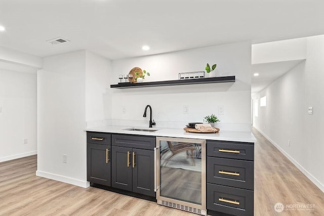 bar with light wood finished floors, beverage cooler, visible vents, a sink, and indoor wet bar