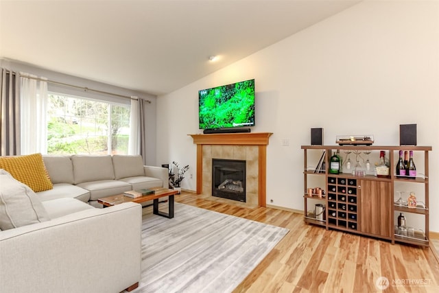 living area with lofted ceiling, a tiled fireplace, and wood finished floors