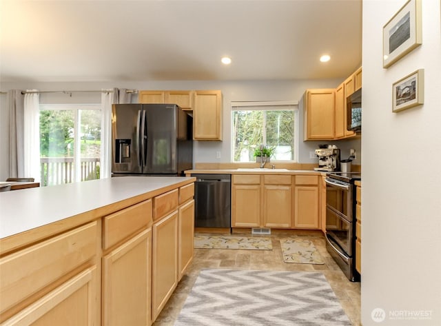 kitchen featuring dishwasher, light brown cabinetry, fridge with ice dispenser, and range with two ovens