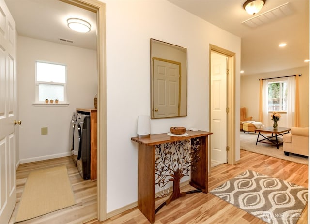 hall with washer and dryer, visible vents, and light wood finished floors