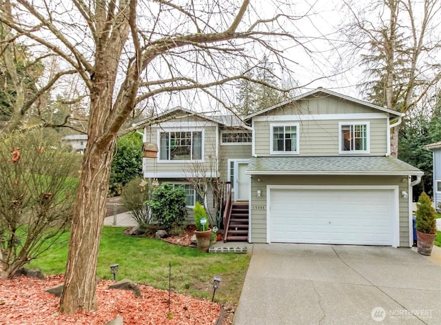 raised ranch with a shingled roof, an attached garage, board and batten siding, a front yard, and driveway