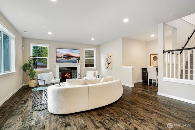 living room featuring recessed lighting, baseboards, a lit fireplace, stairway, and dark wood finished floors