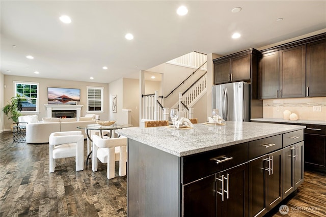 kitchen featuring a warm lit fireplace, open floor plan, dark wood-type flooring, freestanding refrigerator, and recessed lighting