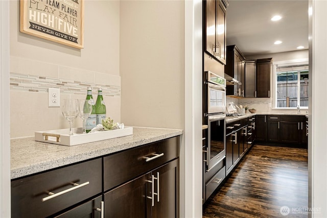 kitchen with dark wood finished floors, decorative backsplash, dark brown cabinets, double oven, and recessed lighting