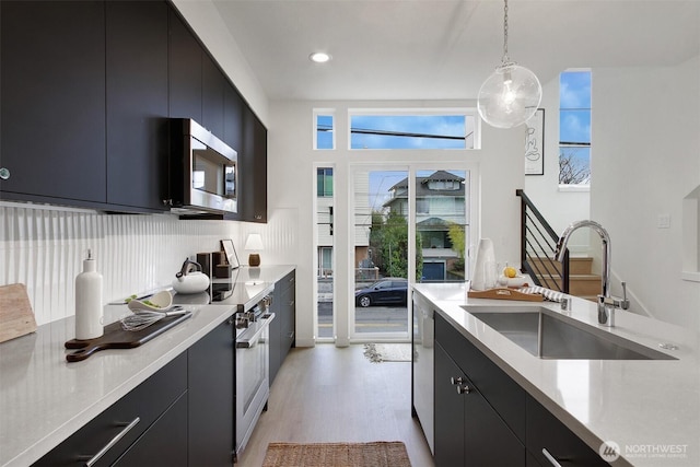 kitchen with stainless steel appliances, light countertops, hanging light fixtures, a sink, and dark cabinetry