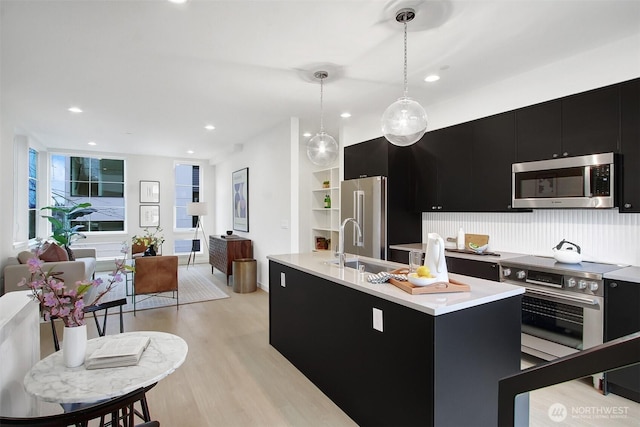 kitchen featuring light wood finished floors, stainless steel appliances, light countertops, open floor plan, and dark cabinetry