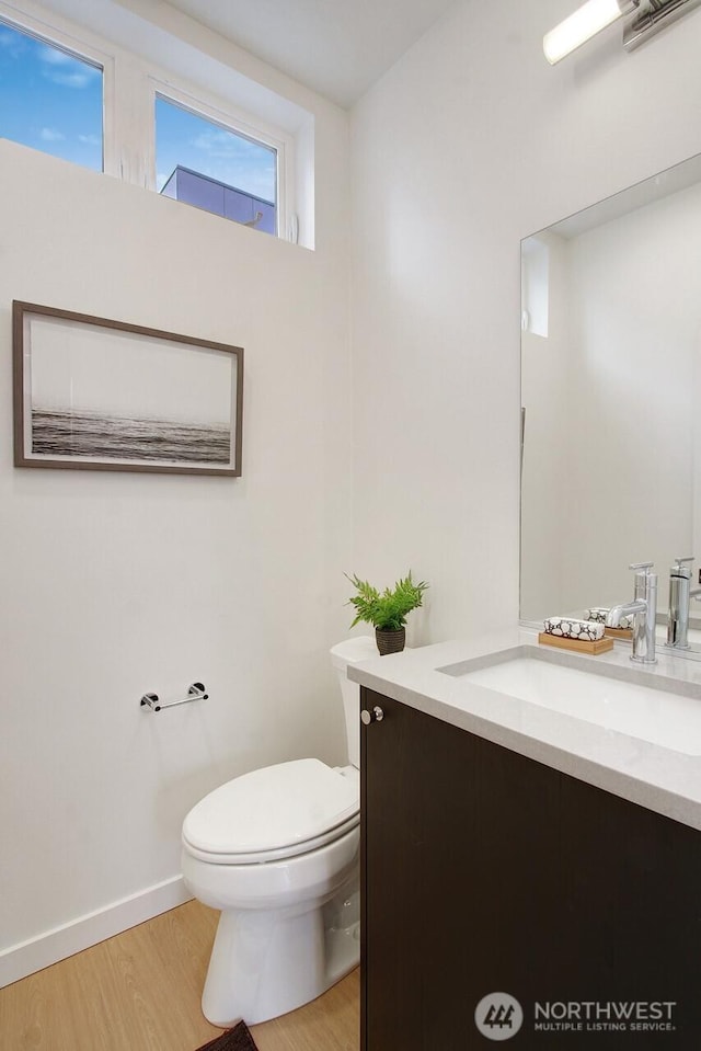 half bath with vanity, wood finished floors, toilet, and baseboards