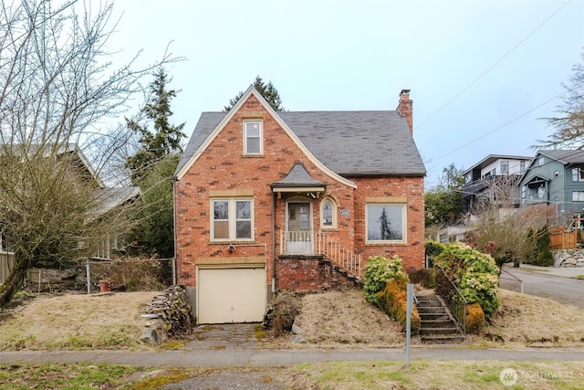 tudor home with a garage, a chimney, and brick siding