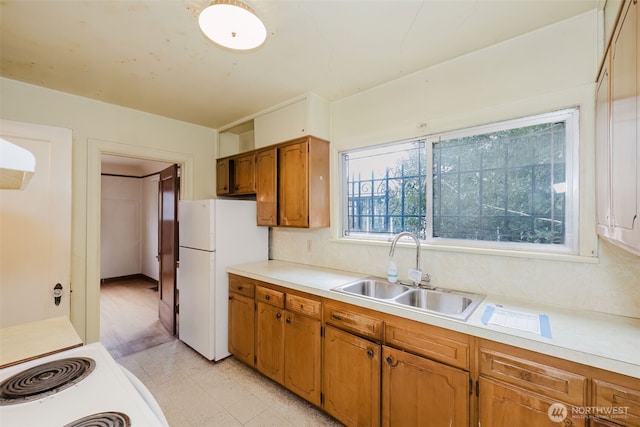 kitchen with light countertops, freestanding refrigerator, brown cabinets, and a sink