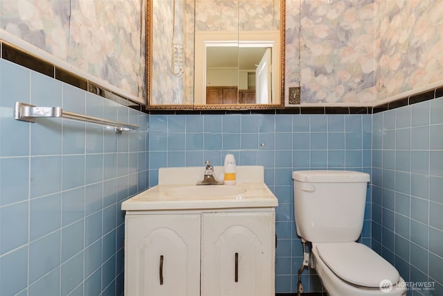 bathroom with wainscoting, vanity, toilet, and wallpapered walls