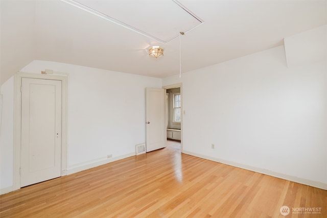 unfurnished room featuring light wood-type flooring, attic access, visible vents, and baseboards