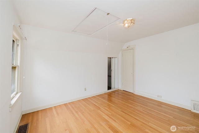 spare room featuring light wood finished floors, attic access, visible vents, baseboards, and lofted ceiling