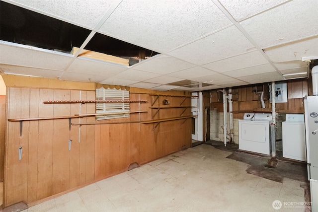 finished below grade area with wood walls, a drop ceiling, electric panel, and washer and dryer