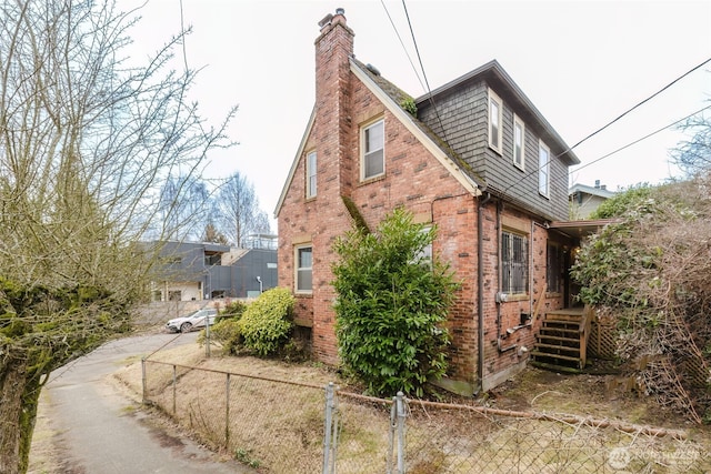 view of property exterior featuring brick siding, a chimney, and fence private yard