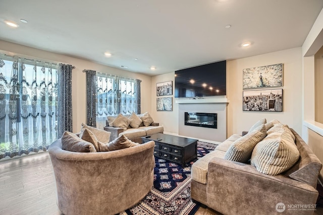 living area with a glass covered fireplace, recessed lighting, and wood finished floors