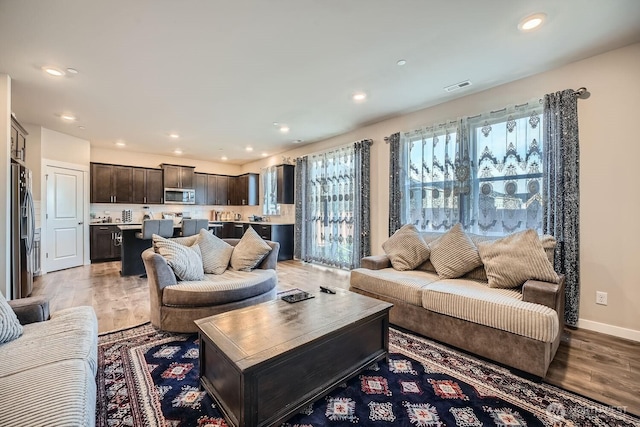 living room with baseboards, light wood-style flooring, visible vents, and recessed lighting