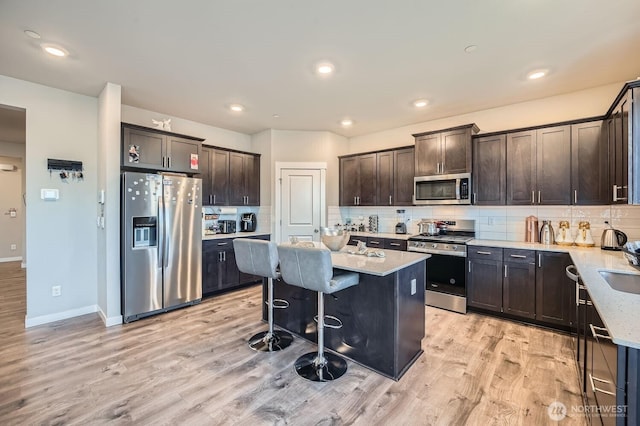 kitchen with dark brown cabinetry, stainless steel appliances, decorative backsplash, and light wood finished floors