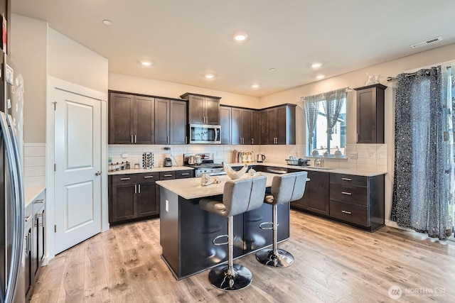 kitchen featuring appliances with stainless steel finishes, visible vents, light wood-style floors, and dark brown cabinets