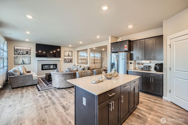 kitchen featuring recessed lighting, light wood-style floors, stainless steel refrigerator with ice dispenser, a center island, and a glass covered fireplace