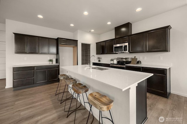 kitchen featuring light wood finished floors, a sink, appliances with stainless steel finishes, a breakfast bar area, and light countertops