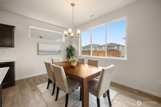 dining space featuring baseboards, visible vents, light wood finished floors, and a chandelier