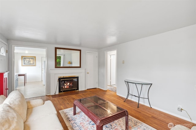 living room featuring wood finished floors, a glass covered fireplace, and baseboards