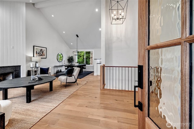 living room featuring beam ceiling, a notable chandelier, a fireplace, high vaulted ceiling, and light wood-type flooring