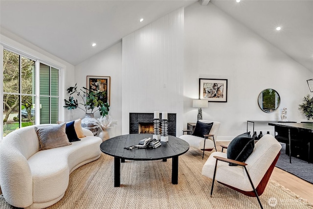 living area with light wood-style floors, recessed lighting, a warm lit fireplace, and high vaulted ceiling