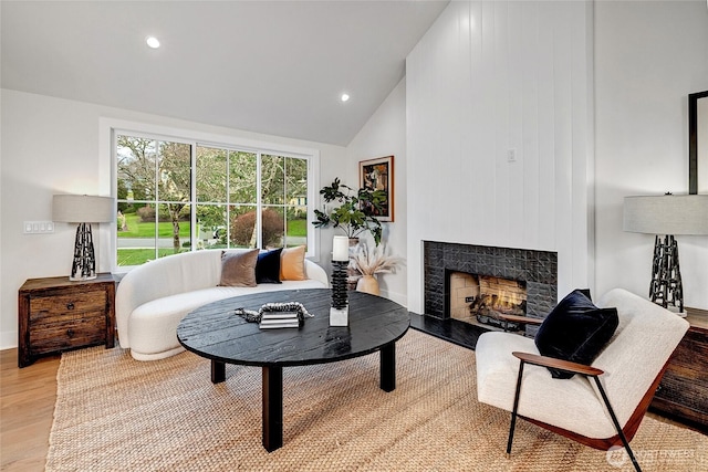 living room with high vaulted ceiling, recessed lighting, wood finished floors, baseboards, and a lit fireplace