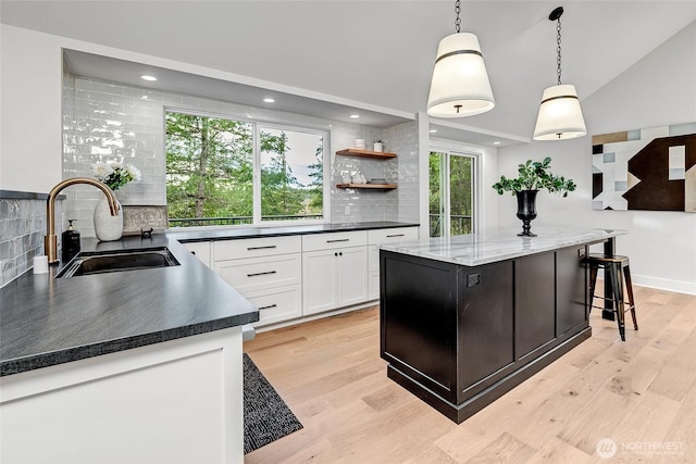 kitchen with light wood finished floors, pendant lighting, white cabinets, and a sink