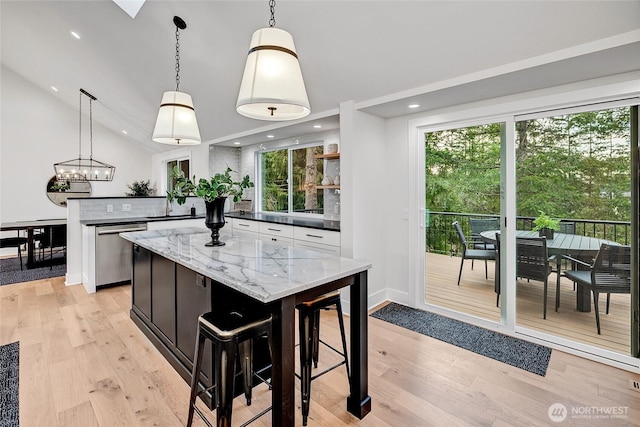 kitchen featuring vaulted ceiling, stainless steel dishwasher, a sink, and light wood-style flooring