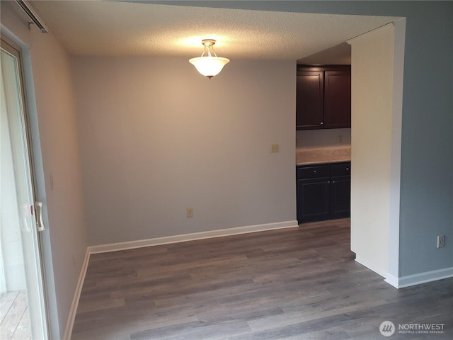 unfurnished dining area featuring a textured ceiling, baseboards, and wood finished floors