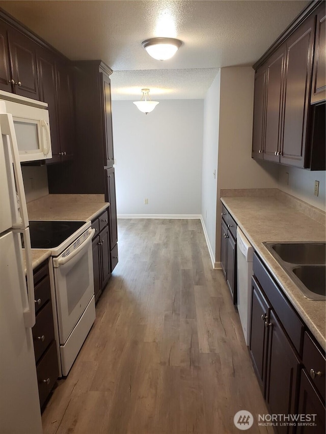 kitchen featuring a textured ceiling, white appliances, a sink, light wood-style floors, and dark brown cabinets