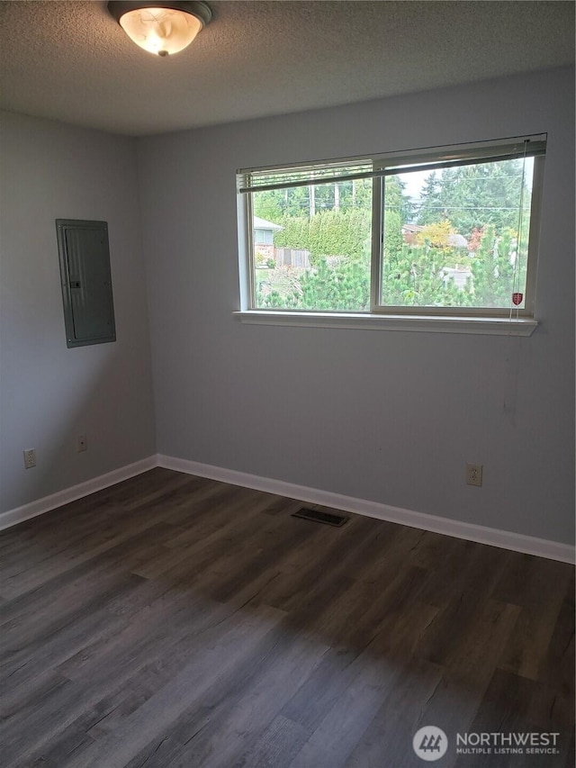 empty room with dark wood-style floors, visible vents, a textured ceiling, electric panel, and baseboards