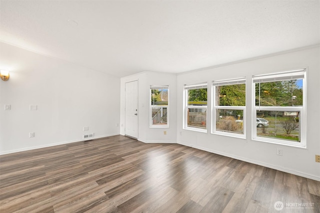 empty room featuring wood finished floors, visible vents, and baseboards